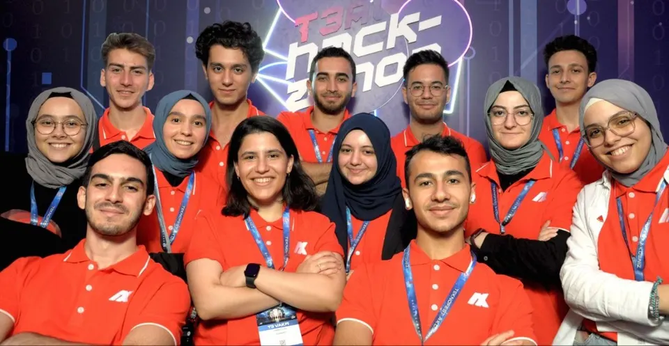 Group of people in red polo shirts and lanyards posing in front of a hackathon event backdrop
